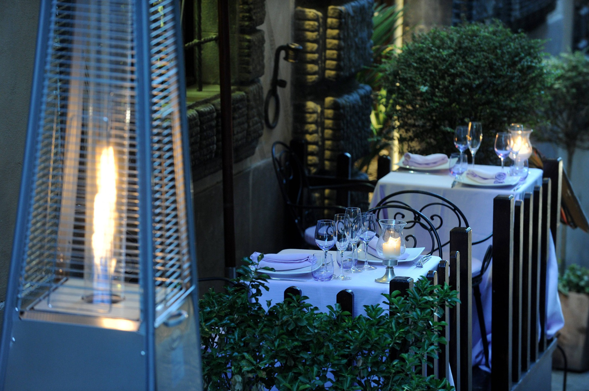 An evening terrace with a lit flame heater and tables laid and waiting — the experience prepared before the first guest arrives.