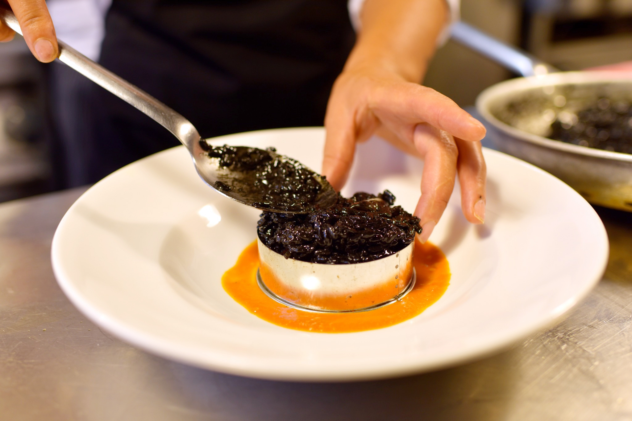 Hands plating a dish element by element — deliberate selection, hierarchy and execution.